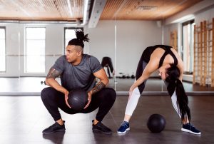 un homme accroupi avec ballon et femme penchée en avant dans une salle de gym