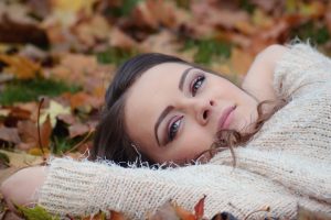 femme allongée dans l'herbe avec des feuilles mortes et un pull blanc