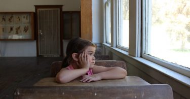 fille assise a une table de classe accoudée et regardant par la fenetre