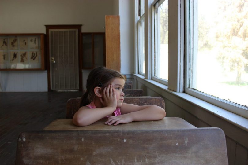 fille assise a une table de classe accoudée et regardant par la fenetre