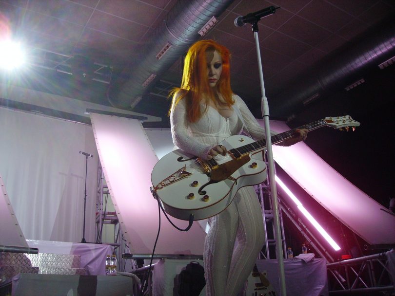 femme rousse en combinaison blanche jouant de la guitare