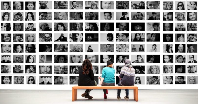 trois personnes assises sur un banc en bois devant des photos en noir et blanc